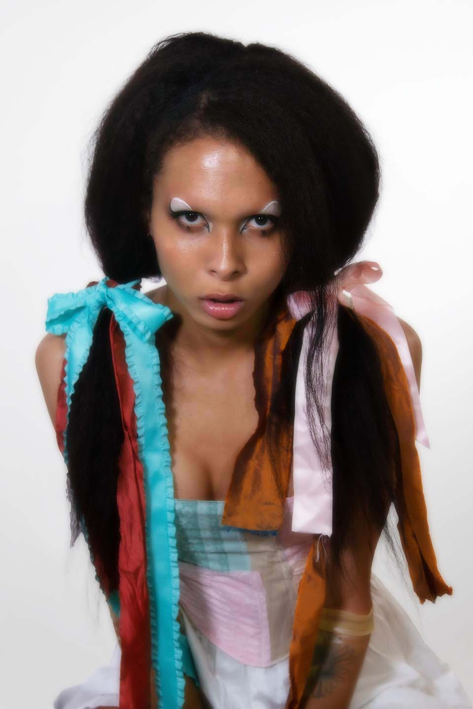 Alessa facing the camera with graphic black eyeliner on wearing a pastel corset and ribbons in her hair against a white background
